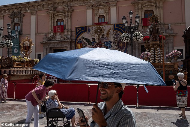 SPAIN: A man carries a parasol as he walks in the Plaza de la Virgen where Corpus Christi sculptures are on display as parts of Spain experience a heatwave on June 21, 2025 in Valencia, Spain