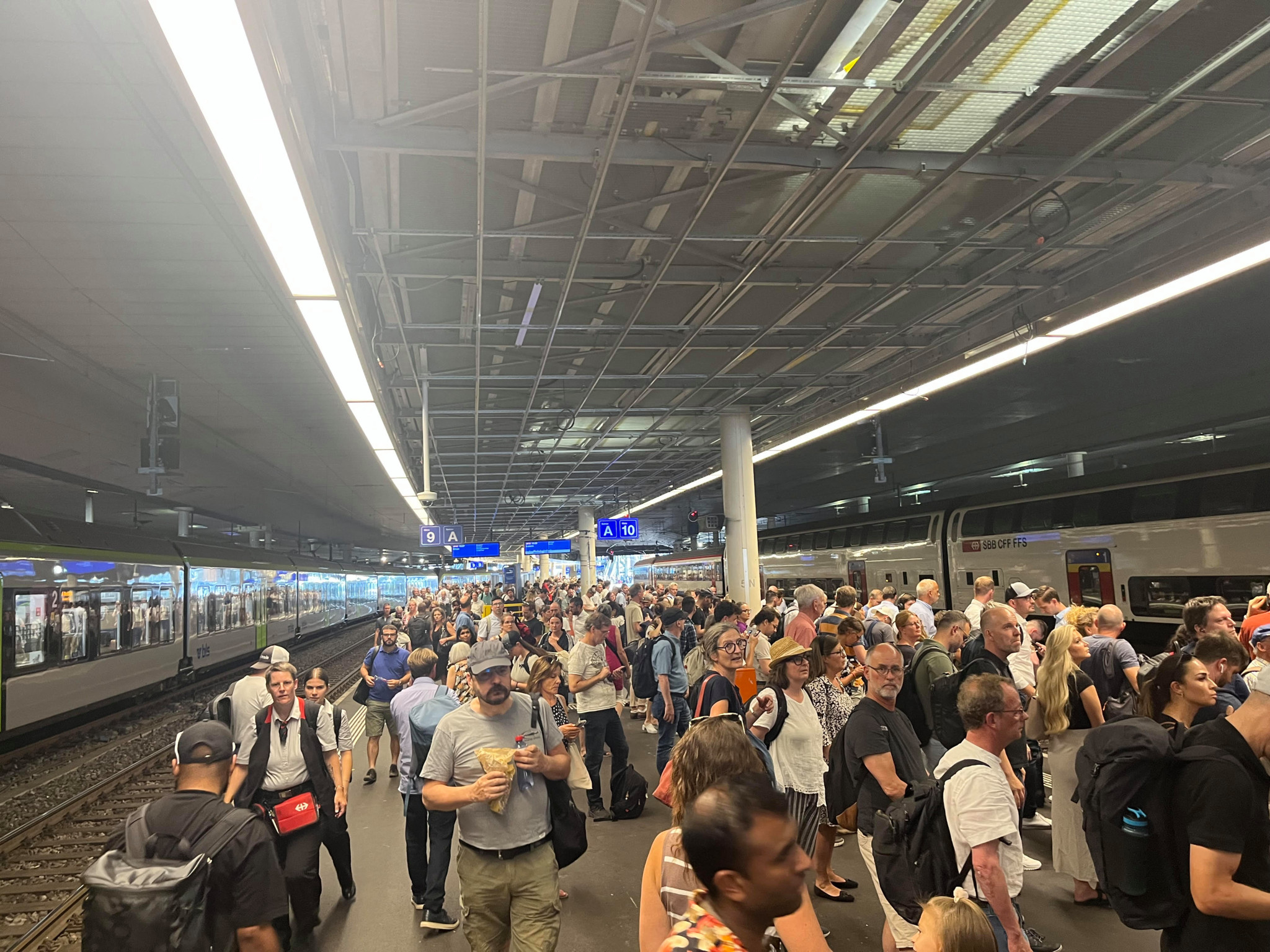 Menschenmenge auf einem belebten Bahnhof, umgeben von Zügen unter einem überdachten Bahnsteig. Menschenmenge auf einem belebten Bahnhof, umgeben von Zügen unter einem überdachten Bahnsteig.