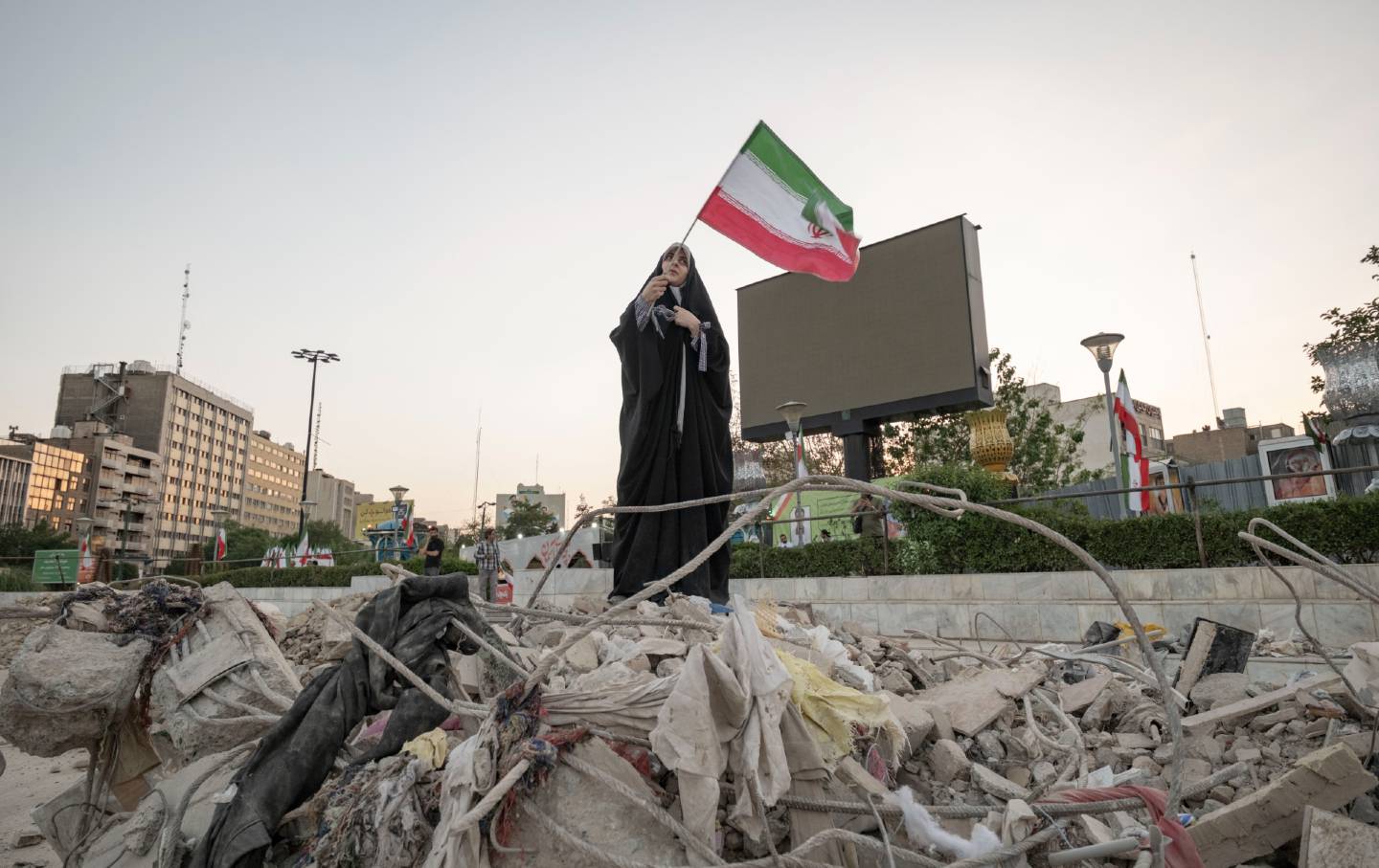 A veiled Iranian art student waves a country flag while standing on symbolic debris of a destroyed building as she performs in an anti-war conceptual play at a square in downtown Tehran, Iran, on June 21, 2025.