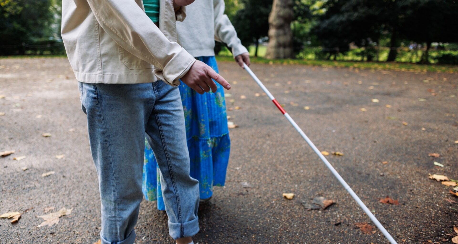 Visually impaired woman with white cane in park being guided by young man