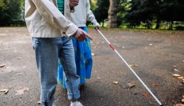 Visually impaired woman with white cane in park being guided by young man