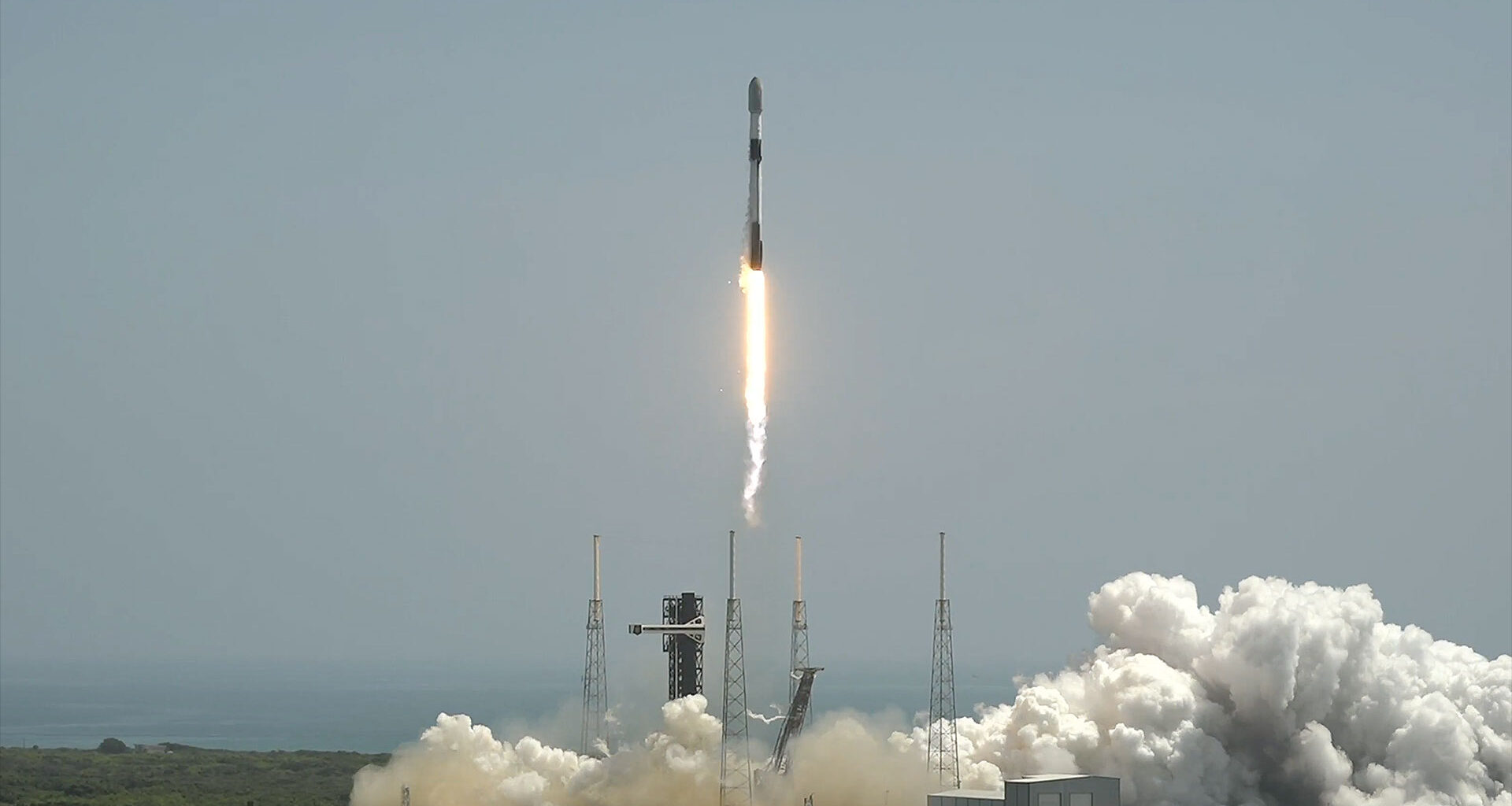 a white and black rocket lifts off into a daytime sky generating a bright flame and a white plume