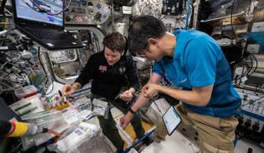 a Japanese man wearing a blue polo and khaki pants and an American woman wearing a black shirt and blue slacks work to draw and collect blood from themselves aboard a space station