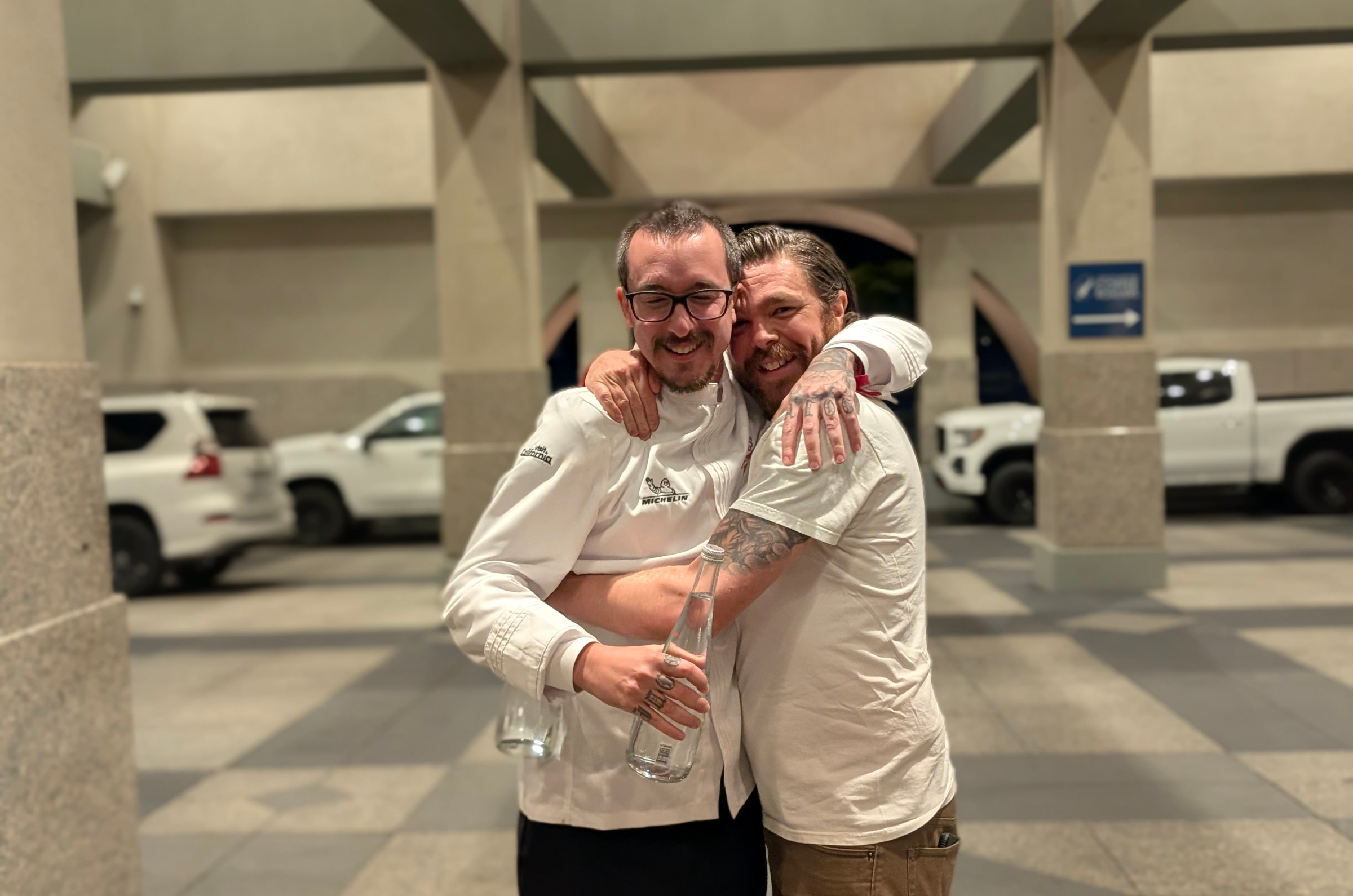 Two white male chefs embrace.