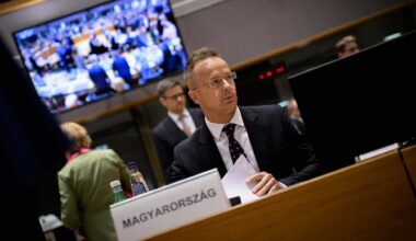 Hungarian foreign minister Peter Szijjartó seated, backdrop of television showing other Council of the EU members getting seated