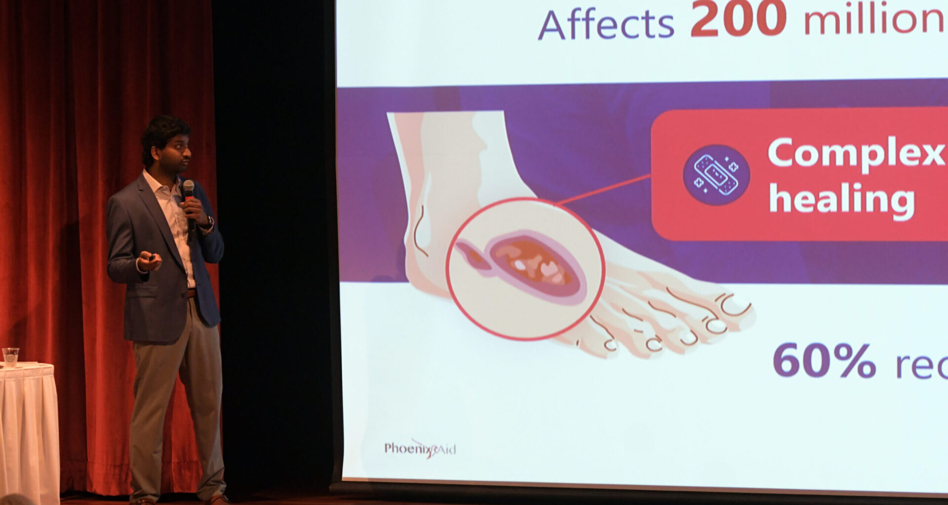 A man gives a presentation about diabetic foot ulcers, showing a slide with affected foot illustration and statistics on chronic wounds.