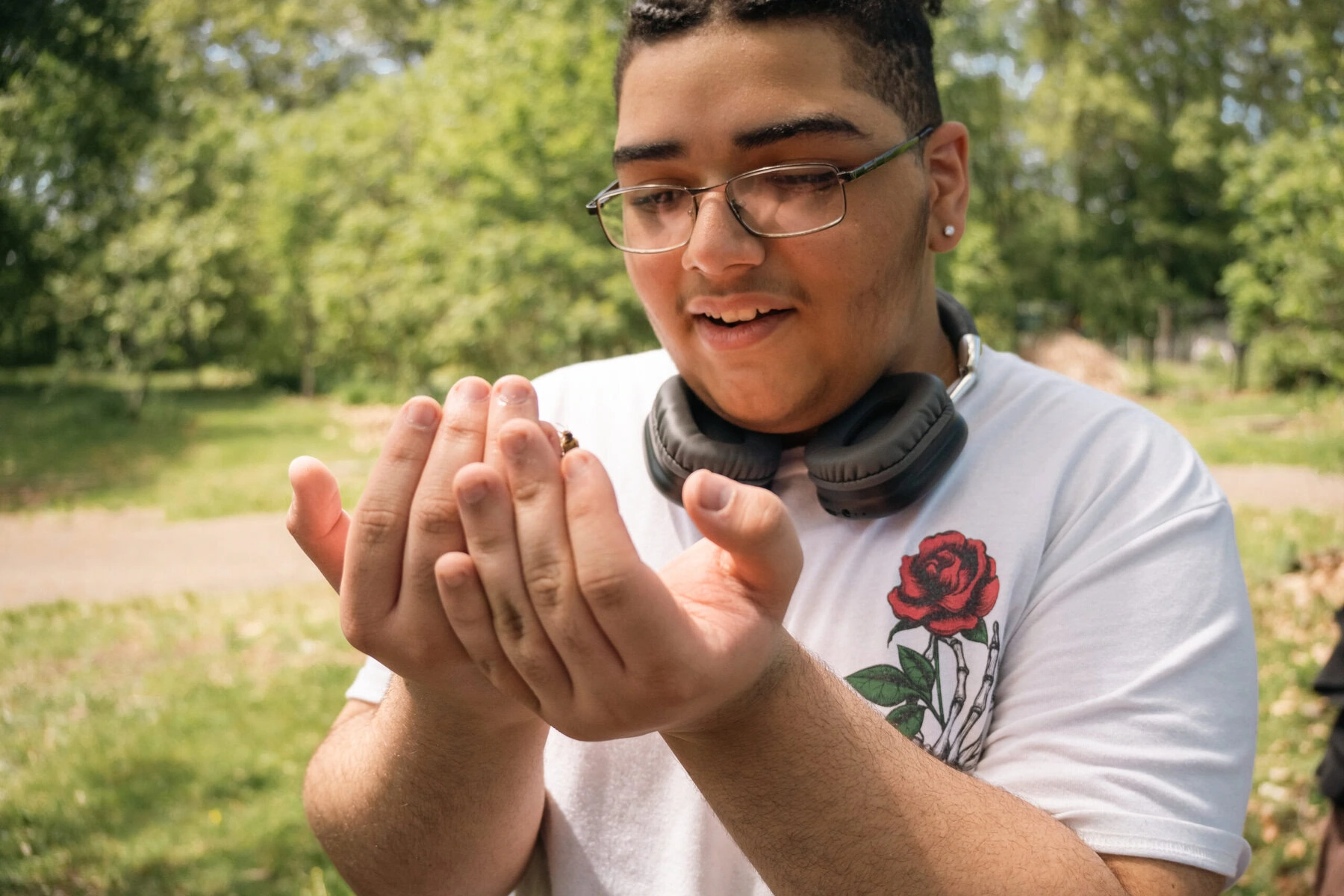 Ray, 16, admires a drone bee after a hive check. He wears glasses and headphones around his neck and is looking at the bee in his cupped hands.