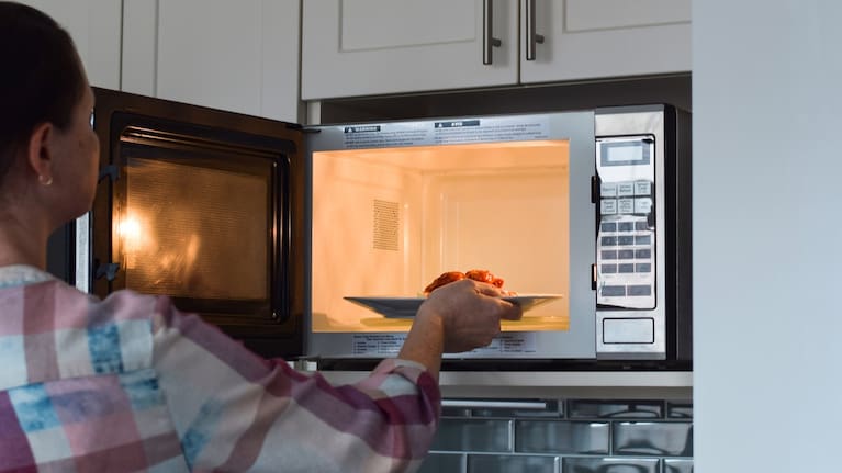 A woman heats her leftovers in the microwave. 