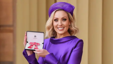 PA Media Dancer and television presenter Amy Dowden wears a purple dress and hat after being made an MBE (Member of the Order of the British Empire) during an Investiture ceremony at Buckingham Palace on 18 February, 2025.