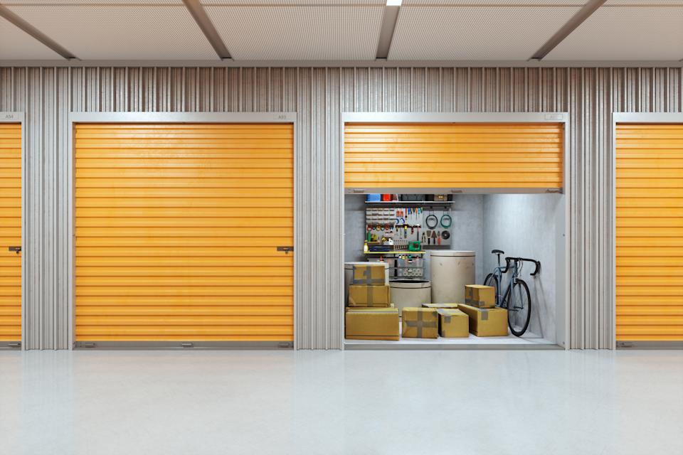 Storage unit with open door showing stacked boxes, a bicycle, and tools hanging on the wall