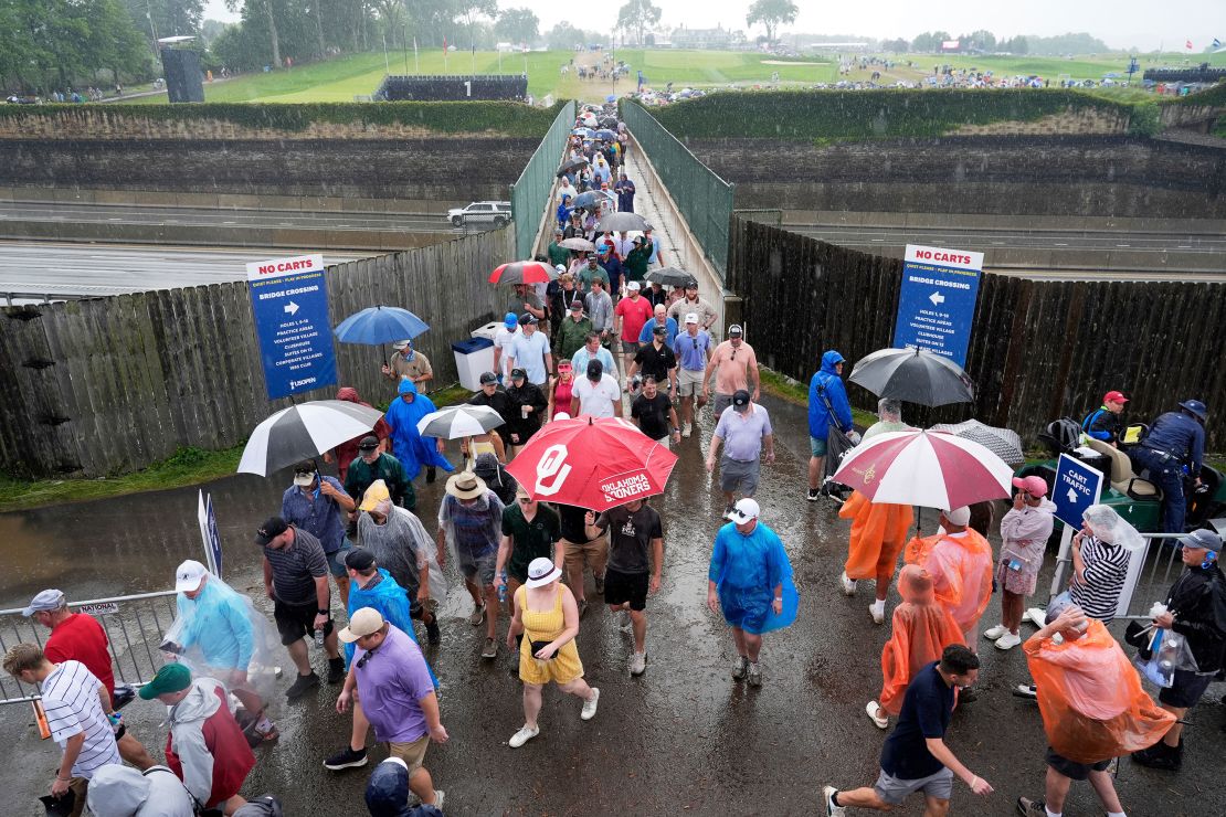 Spectators use umbrellas as they cross a pedestrian bridge during a weather delay.