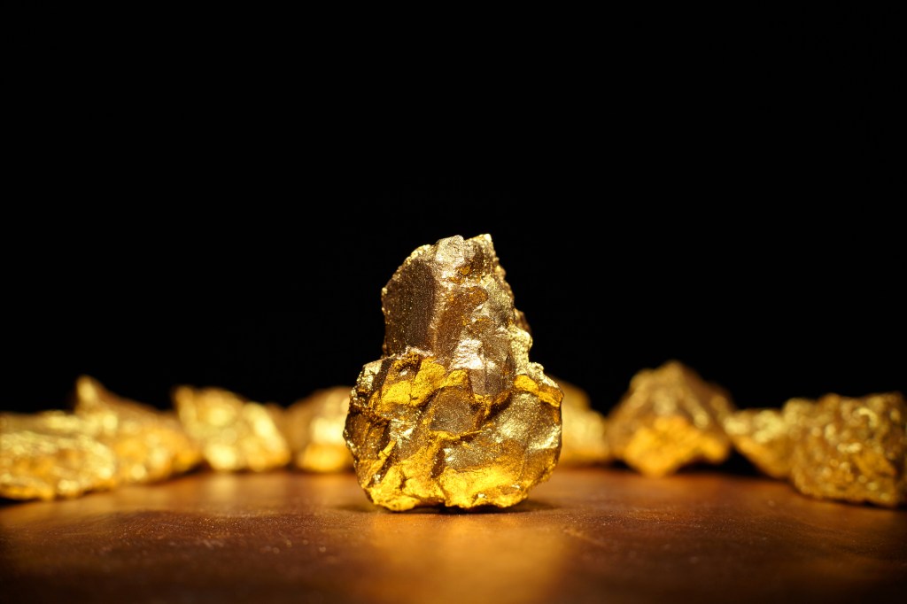 Close-up of a large gold nugget with smaller nuggets in the background.