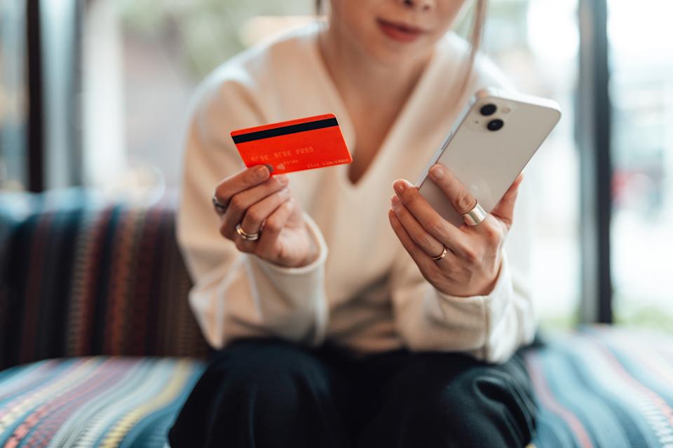 Person holding a smartphone and a credit card, sitting on a striped cushion
