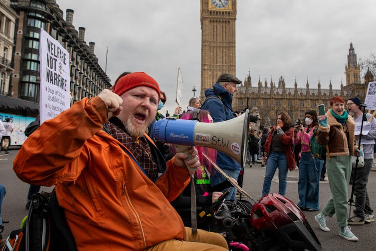 A protestor shouting into a loud speaker in front of the houses of parliament in London.
