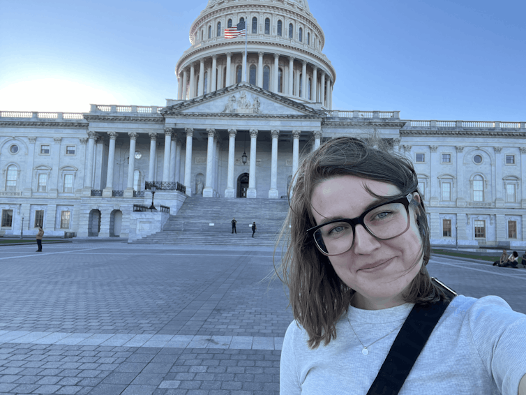 A woman in glasses standing in the foreground of the US Capitol building, Washington DC.