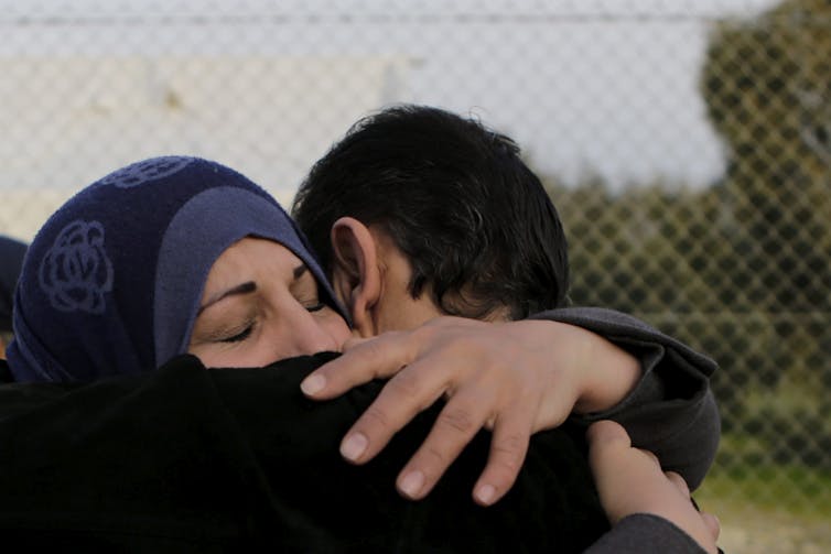 A woman wearing a headscarf hugs a man