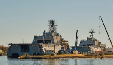The ships are surrounded by cranes and scaffolding, with a clear sky in the background