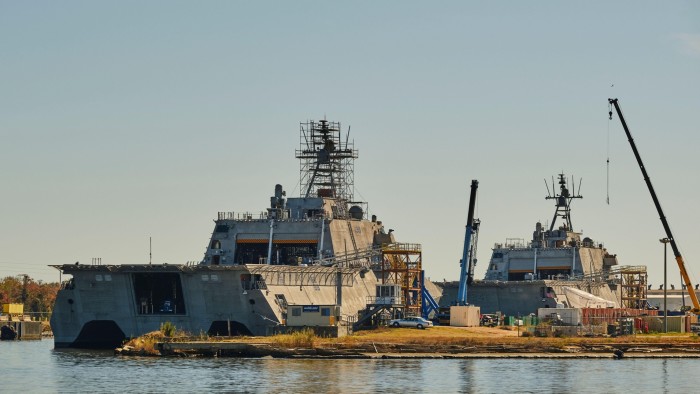 The ships are surrounded by cranes and scaffolding, with a clear sky in the background