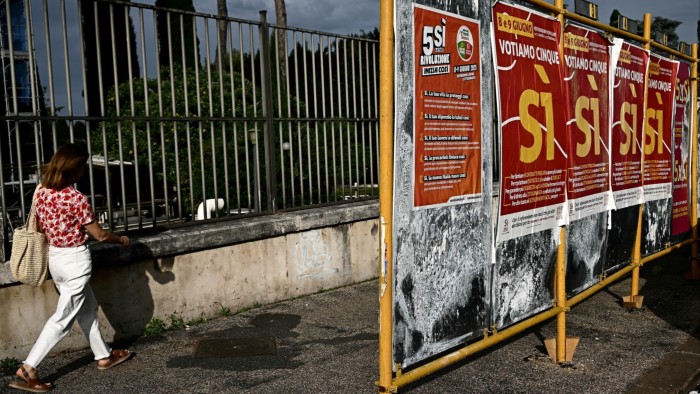 A woman walks past a series of campaign posters in downtown Rome promoting a Yes vote