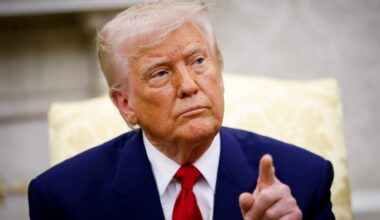 Donald Trump wearing a blue suit over a white shirt with a red. His left index pointer pointing at something to his left