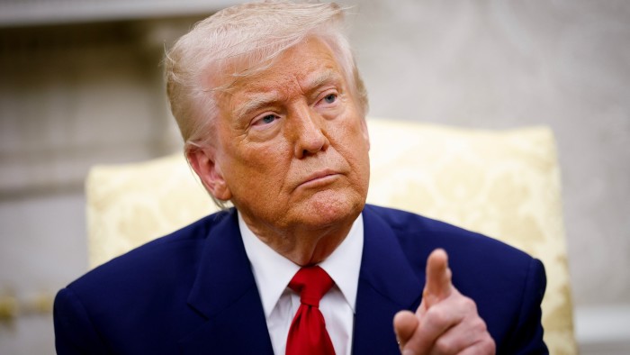 Donald Trump wearing a blue suit over a white shirt with a red. His left index pointer pointing at something to his left