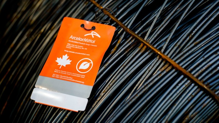 A close-up of a bundle of steel wire, with an orange ArcelorMittal tag attached. The tag indicates the steel is made in Canada from sustainable sources, featuring a maple leaf and leaf symbol