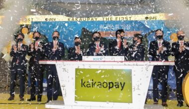 People clapping behind a podium with the Kakao Pay logo on it and confetti in the air at the payments provider’s debut on the Korea Exchange in 2021