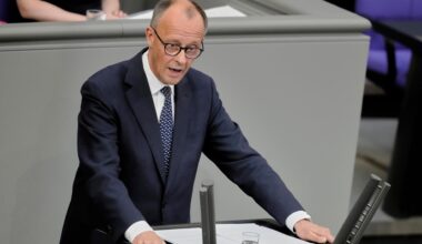 Das Foto zeigt Friedrich Merz am Rednerpult des Bundestags. Er trägt dunkelblauen Anzug und eine blaue Krawatte. Seine Arme stützt er auf das Pult.