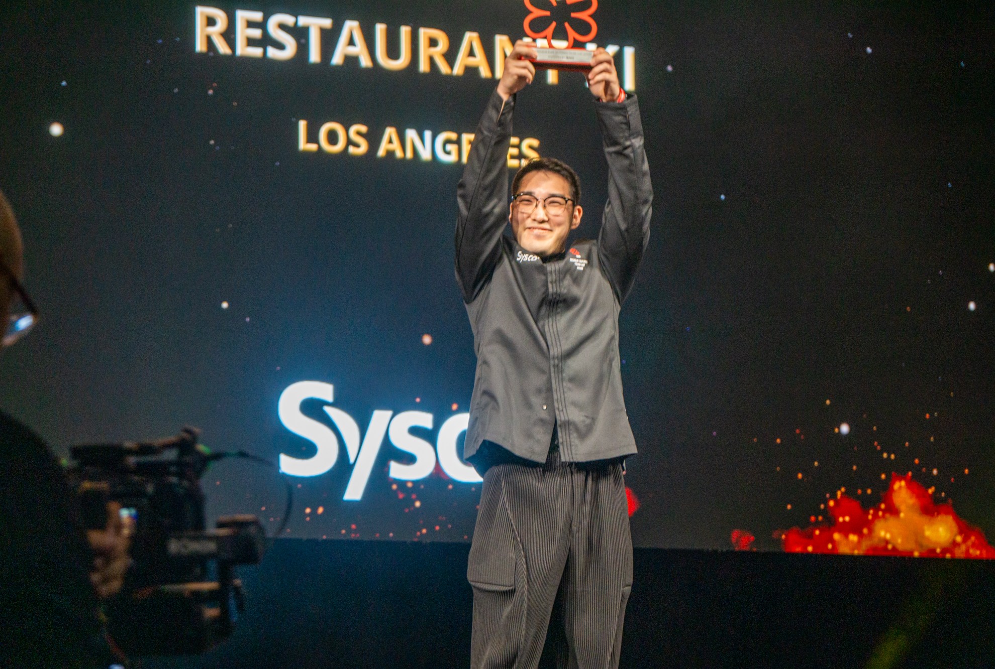 A male Asian chef holds up an award.