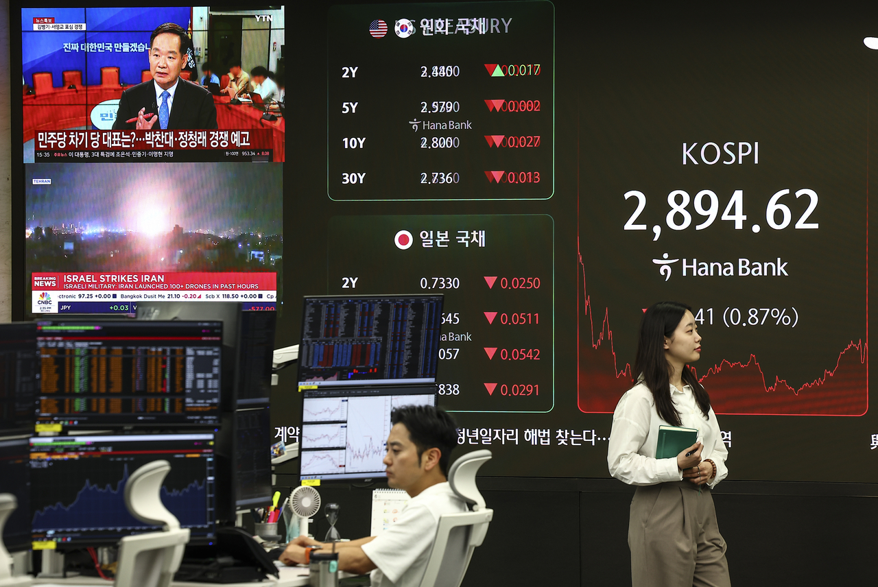 A TV screen on the left shows news about Israel's airstrikes on Iran as the Kospi closes down 0.87 percent on Friday at a dealing room in Hana Bank's headquarters in central Seoul. (Newsis)