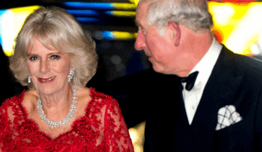 Queen Camilla wearing a red dress and diamonds next to King Charles in a tux
