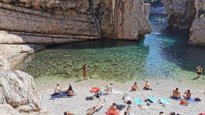 People sunbathe on colorful towels on a rocky shore by a turquoise lagoon