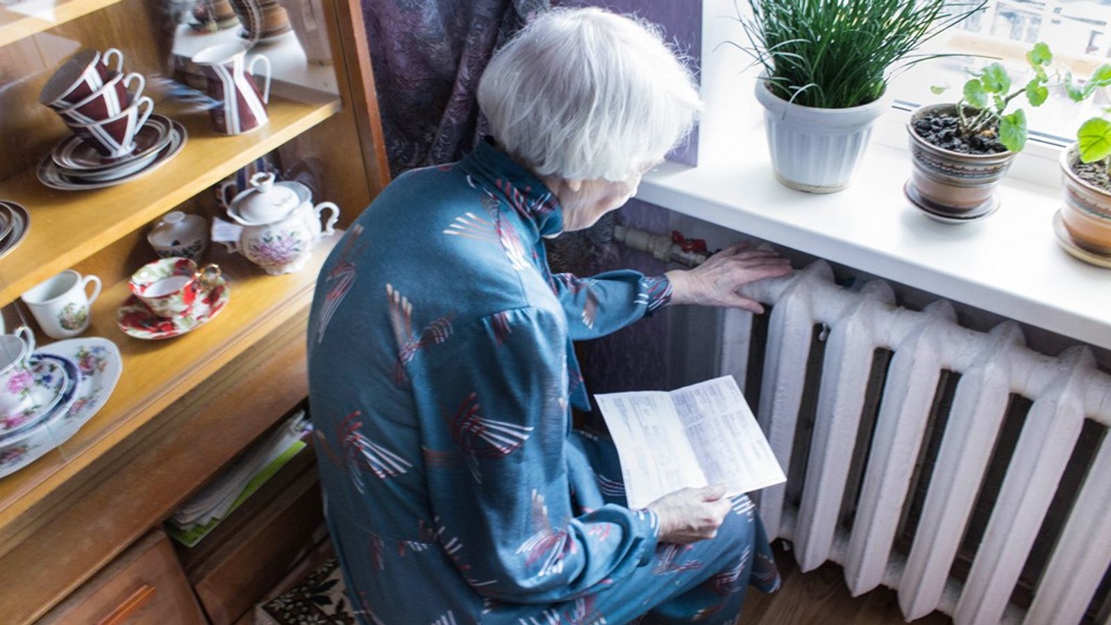 An elderly woman checking the warmth of her radiator. Pic: iStock