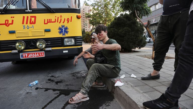 An injured person sits on a roadside in the aftermath of Israeli strikes, in Tehran, Iran.
Pic: Reuters