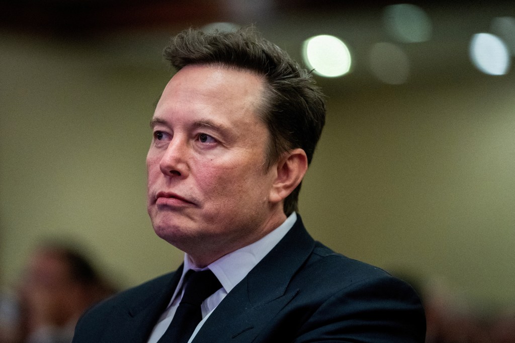 Elon Musk listening to Donald Trump speak at a meeting.