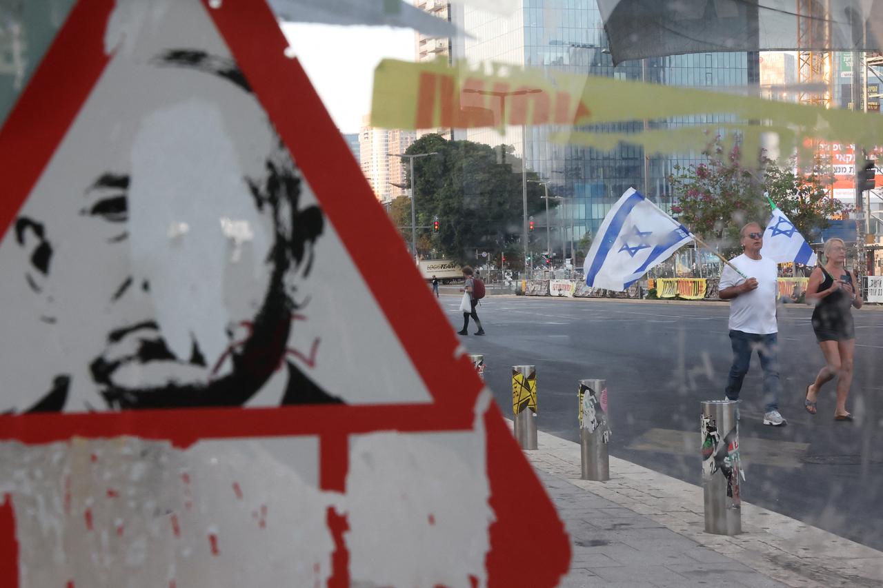 Demonstrators wave the Israeli flag as they walk past a defaced poster of Prime Minister Benjamin Netanyahu during an anti-government protest calling for action to secure the release of Israeli hostages, in front of the Defence Ministry in Tel Aviv on June 7, 2025. (AFP Photo)