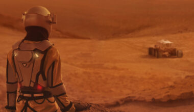 A woman stands to the left of a rover on a red surface