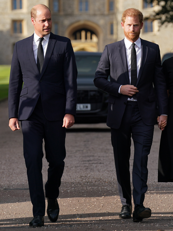 Prince William and Prince Harry walking in dark suits next to each other at Windsor Castle