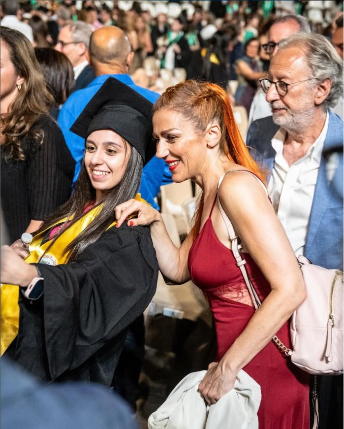 A woman in a red dress congratulates a graduating woman.