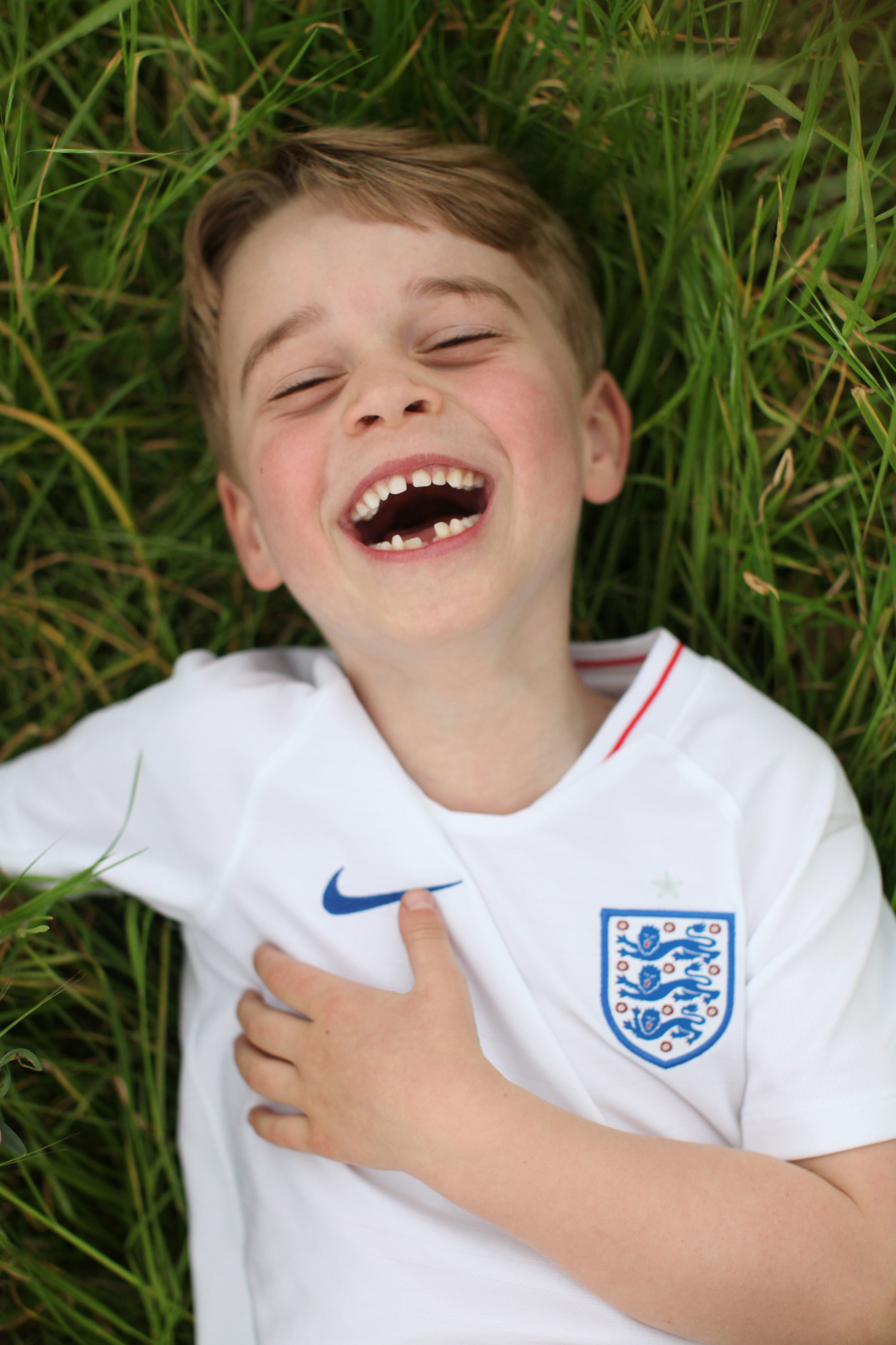 Prince George laughing in the grass wearing an England soccer jersey.