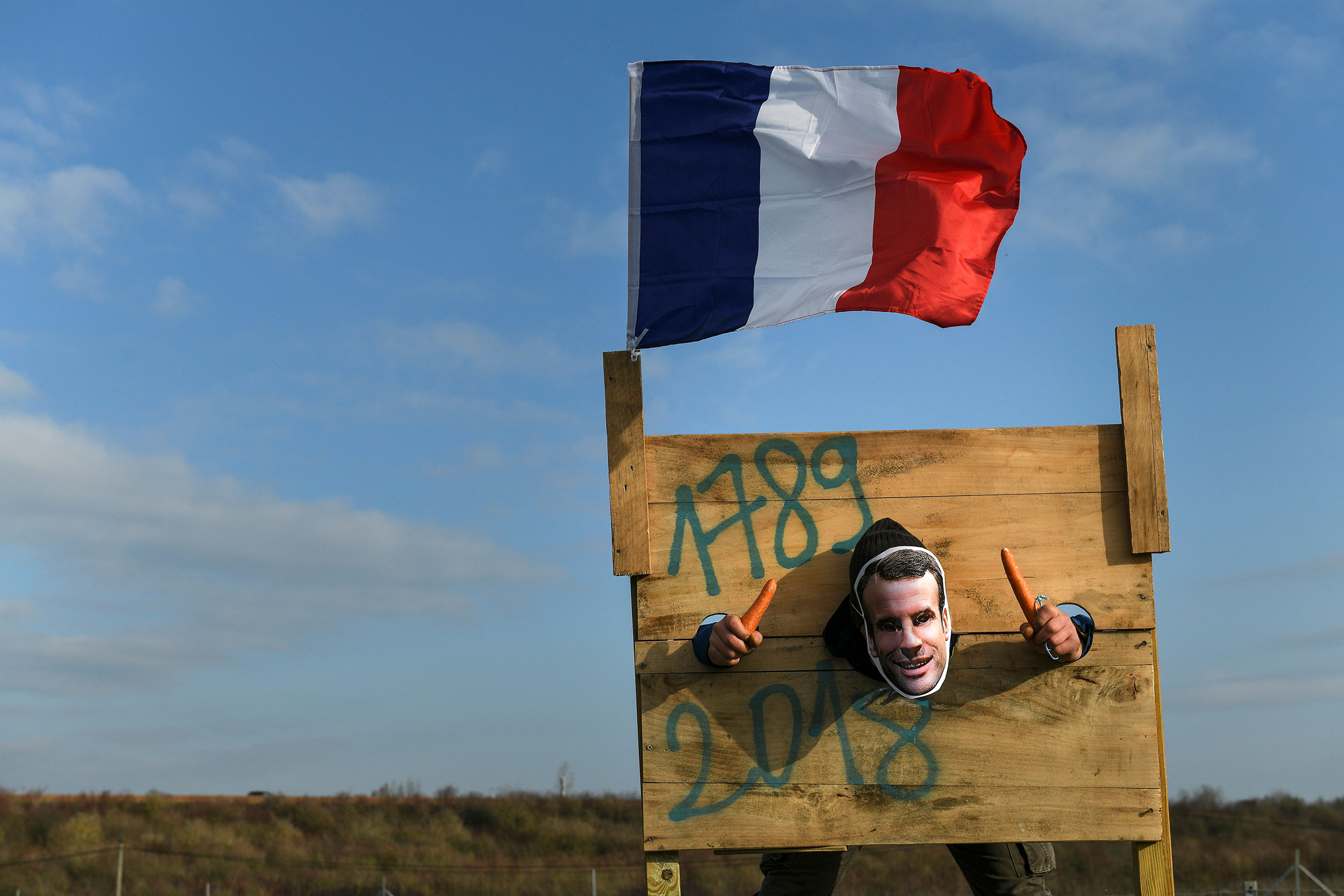 Protestor wearing Emmanuel Macron mask in pillory at Yellow Vests demonstration.