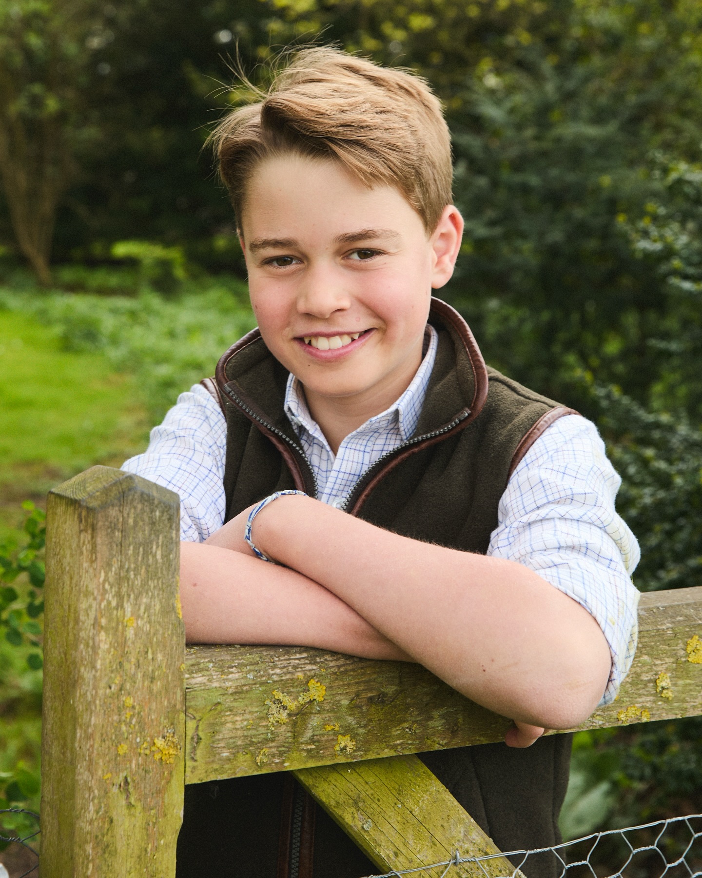 Portrait of a smiling boy leaning on a wooden fence.