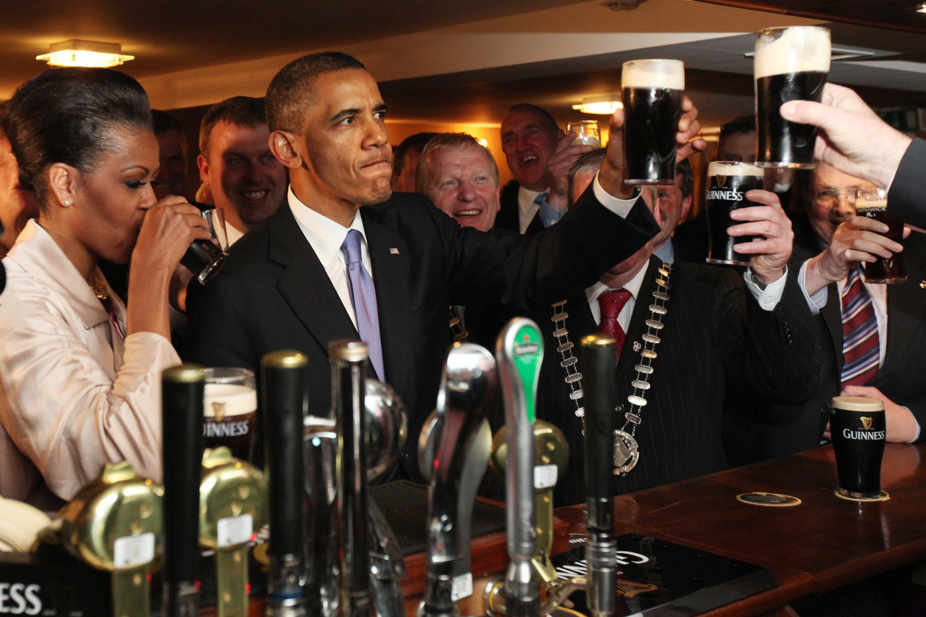 President Barack and Michelle Obama drinking Guinness in an Irish pub with other people.
