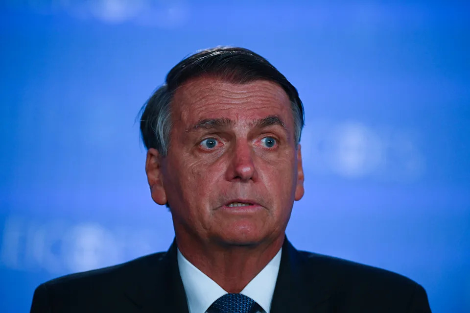 A person in a formal suit speaking at a public event with a serious expression