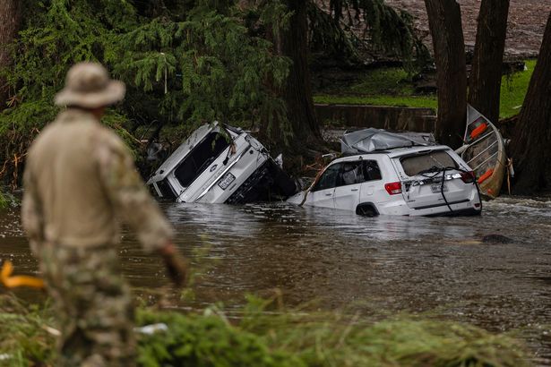Vehicles sit submerged as a search and rescue worker looks through debris for any survivors or remains of people swept up in the flash flooding 