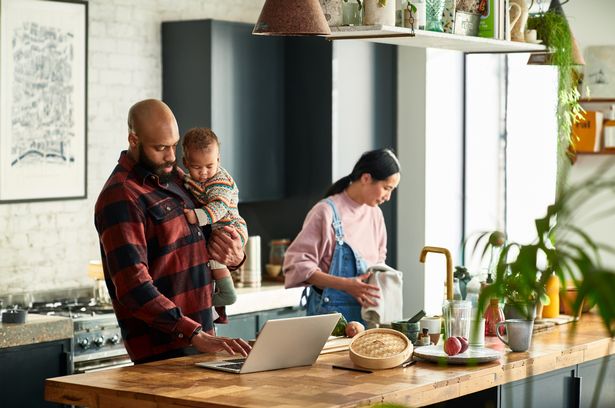 Black father holding baby son and using laptop, watching cooking video online, modern family life, real people