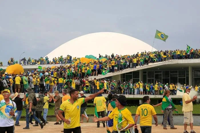 Large crowd of people in Brazil jerseys gathered outside a modern government building, waving Brazilian flags