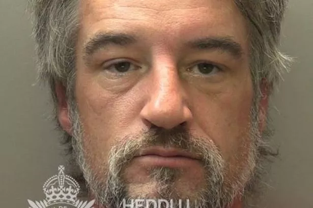 Police mugshot of a man in his late 40s with long greying heard and a greying beard