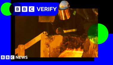 Worker in a steel plant wearing protective headgear and a reflective visor stands behind some molten metal. The BBC Verify branding appears in the top corner.