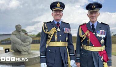 Two men in navy blue army suits. They are standing next to a stone statue of a person sitting down.
